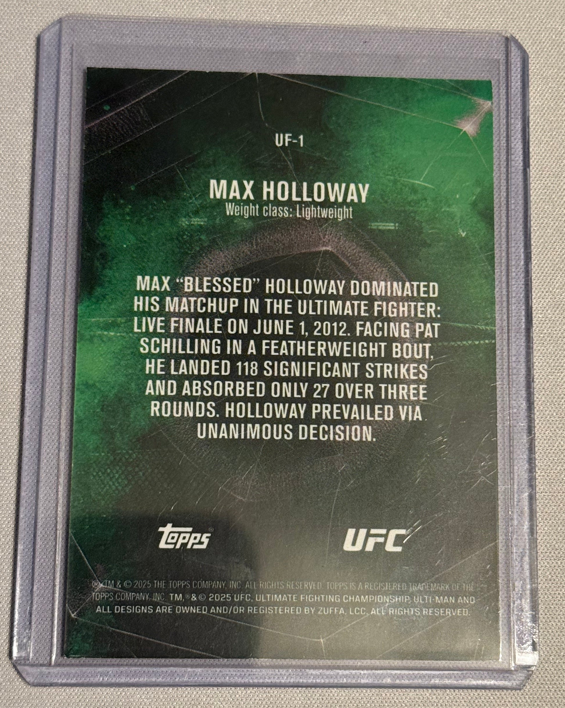 A UFC trading card featuring Max Holloway, encased in a clear protective plastic sleeve, photographed on a light beige fabric background.
